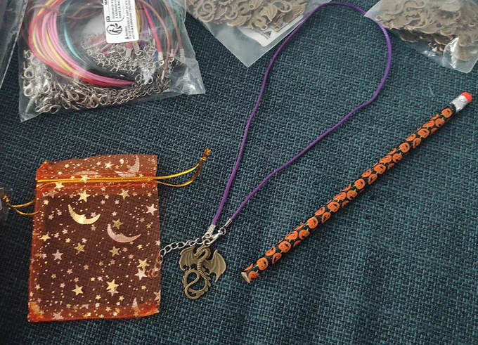 Regalos! El collar de dragón con una cinta morada. Un lápiz con calabazas. Una bolsita naranja de regalo para el colgante.