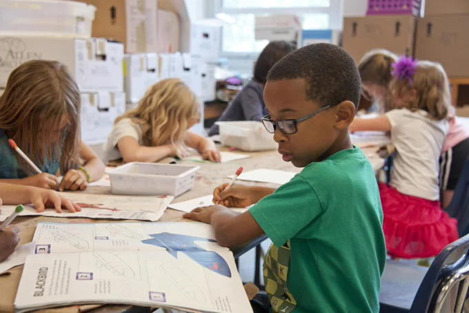 Group of primary school age children sat at a long table, getting on with their work