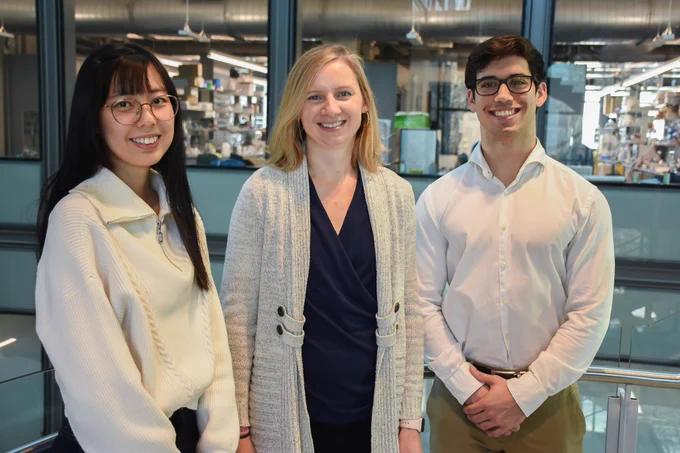 Full-color photo of grad student, PI, and undergrad standing in Frick Lab with labs in background. (Photo M. Saghafi.)