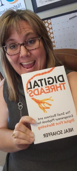 Jennifer is holding a copy of a book titled "Digital Threads" written by Neal Schaffer. She has a big open smile on her face.