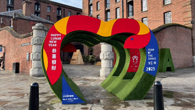 Near the entrance to Anchor Courtyard at Liverpool's Royal Albert Dock, a large heart sculpture decorated with a wooden red and yellow snake stands.
