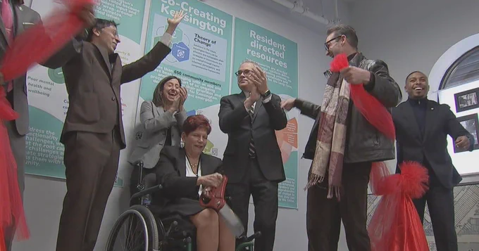 a group of people, one a woman in a wheelchair, celebrate the ceremonial ribbon-cutting 