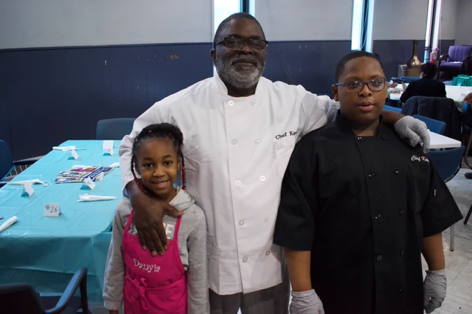 An older man in a chef's hat poses for a picture with two grandchildren.