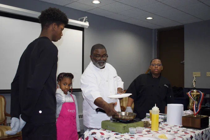 An older man shows three younger children how to set up a portable stove.