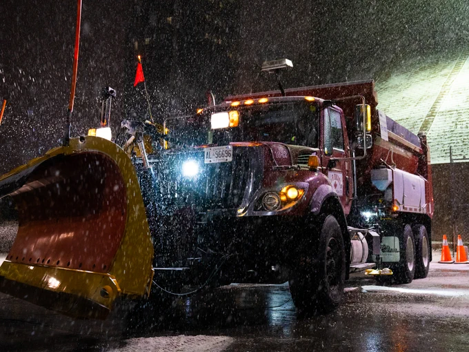 A snow plow in the falling snow at night