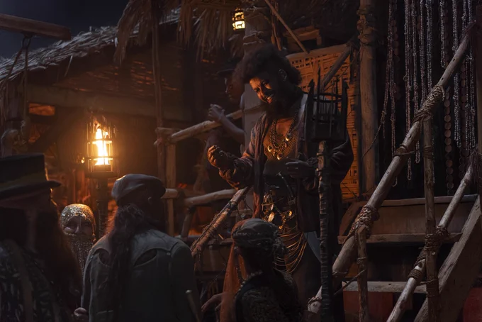 At night, a crowd gathers around torchlit steps to listen to a bejeweled, armed Tanchico local.