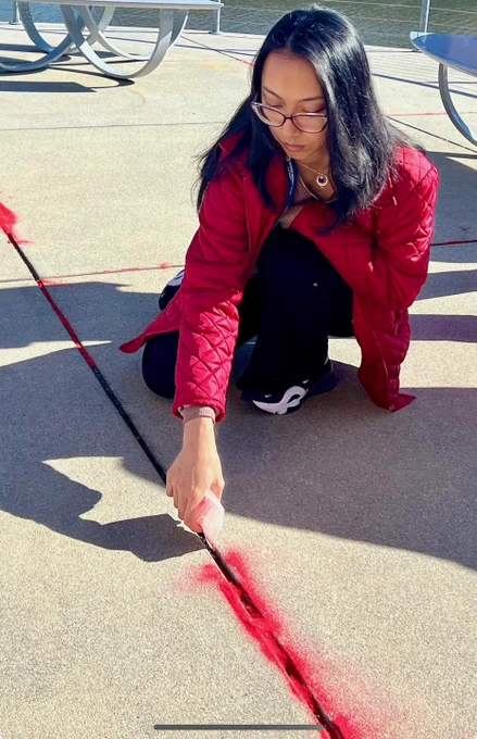 Woman pouring red sand on sidewalk