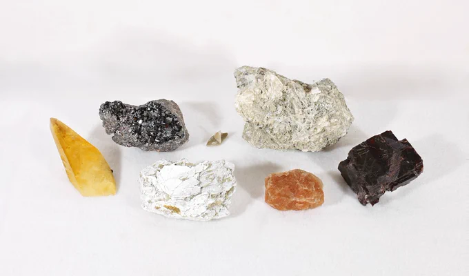 Two rows of mineral specimens. In the front row from left to right are specimens of calcite, gaylussite, sylvite with associated halite, and villiaumite. In the back row from left to right are specimens, of magnetite, thenardite, and trona.