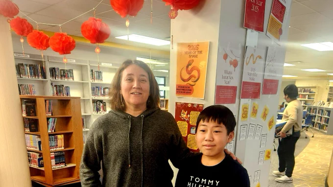 A  student and a teacher standing in a library under a swag of red paper lanterns.