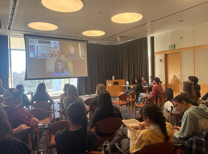 A seated audience faces a screen with virtual panelists.