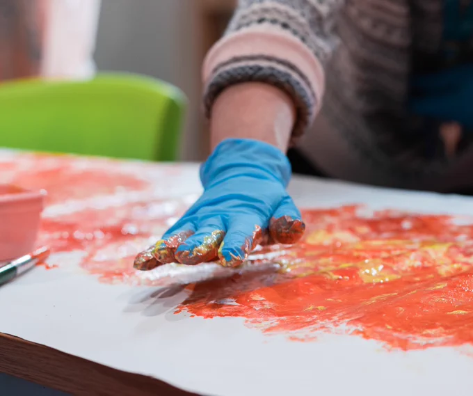 A hand in a blue glove takes part in some finger painting activities