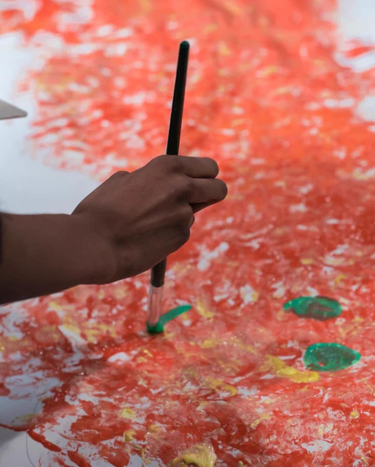 A hand holds a paintbrush, adding a green mouth to a finger painted creature!