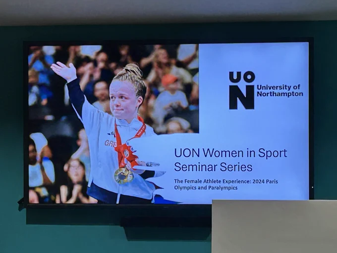 Image shows a screen on which there is image of Maisie Summers-Newton, Paralympic swimmer, on the left and on the right there is a University logo top right and below the logo the screen reads ‘UON Women in Sport Seminar Series. The Female Athlete Experience: 2024 Paris Olympics and Paralympics’