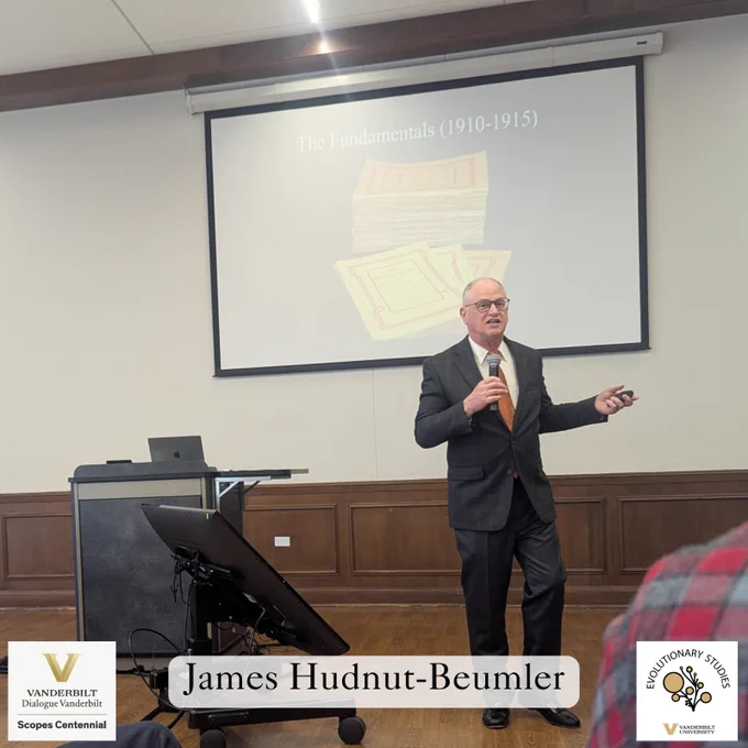 James Hudnut-Beumler, wearing a dark suit with an orange tie, speaks into a microphone while presenting at the Scopes Centennial event at Vanderbilt University. Behind him, a slide titled 'The Fundamentals (1910-1915)' features an image of a stack of booklets. A Vanderbilt Dialogue Vanderbilt and Evolutionary Studies logo are visible on the image.