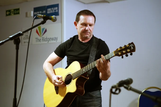 A man playing guitar on stage, focused on his performance during The Beacon open mic night.