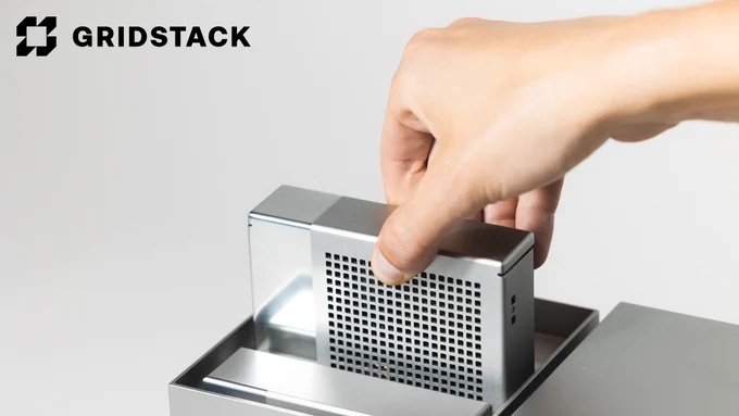 A close-up of a hand inserting a modular storage block into a Gridstack device. The sleek, silver block features a perforated design, emphasizing ventilation and modern aesthetics. The Gridstack logo is displayed in the upper left corner against a clean white background, highlighting the brand’s minimalist and functional design.