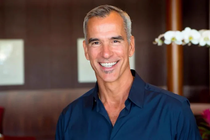 A headshot of director Jerry Mitchell, wearing a blue shirt