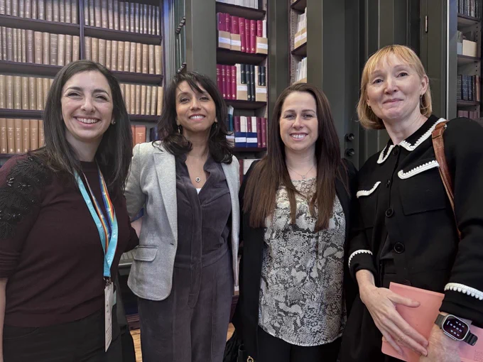 A group of four women smile for a photo, in the RCS England library. 