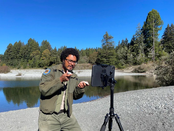 Man in front of iPad near a river. 