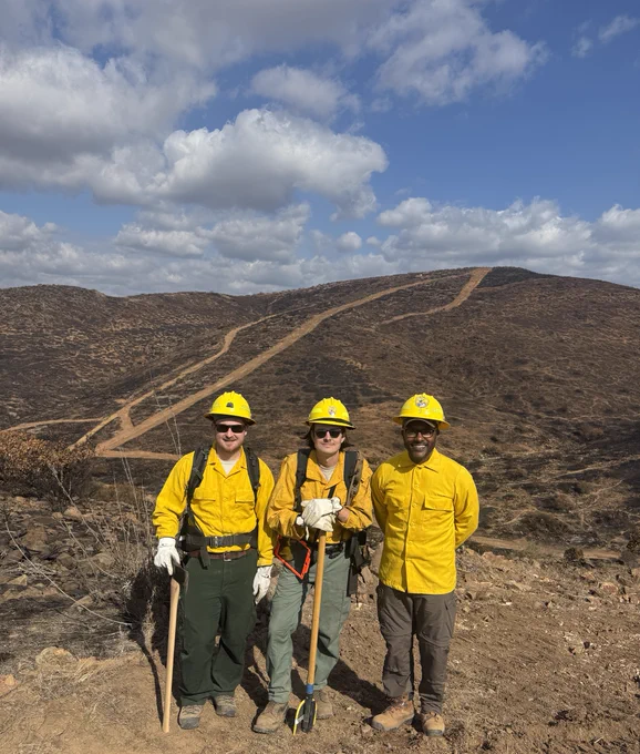 Three Resource Advisors in wildland fire protective clothing smile on a hillside.