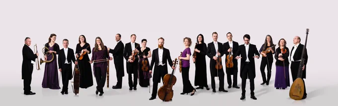 A photograph of a group of well-dressed musicians holding their instruments, posing facing different directions.