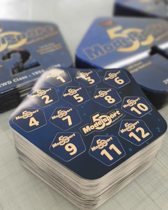 Stack of custom Modelsport branded racing number sticker sheets, together with some of the acrylic trophies produced.