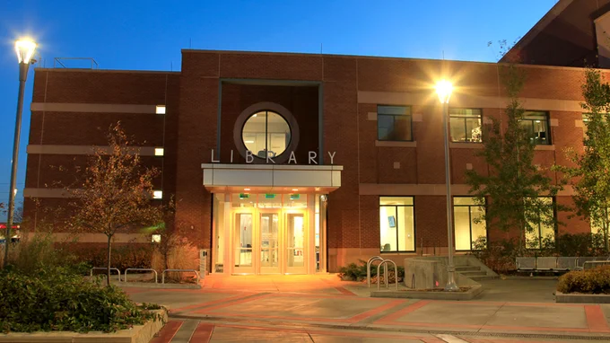 Exterior view of the Galaxie Library building at dusk, illuminated by streetlights, featuring a prominent entrance with the word "LIBRARY" above the doorway.
