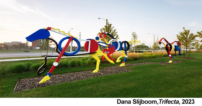 Image of 3 white, black, blue, red and yellow racing horse sculptures in a landscape.