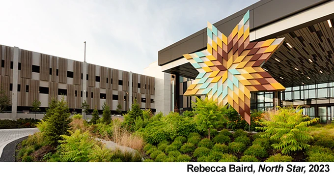 Image showing sculpture of a large multi-coloured 7-point star in a landscape in front of a building.