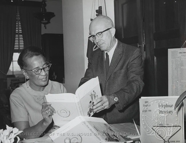 Image of Gus Hawkins with his aide, looking at a book