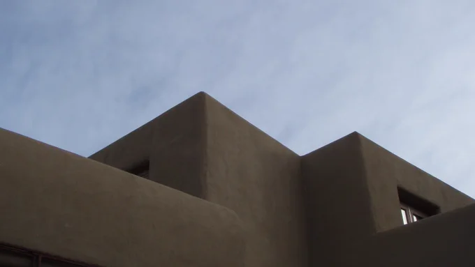 Exterior of the Georgia O'Keeffe Museum. The camera is tilted towards the sky to see only the top corners of an adobe building against a blue sky with light clouds. 