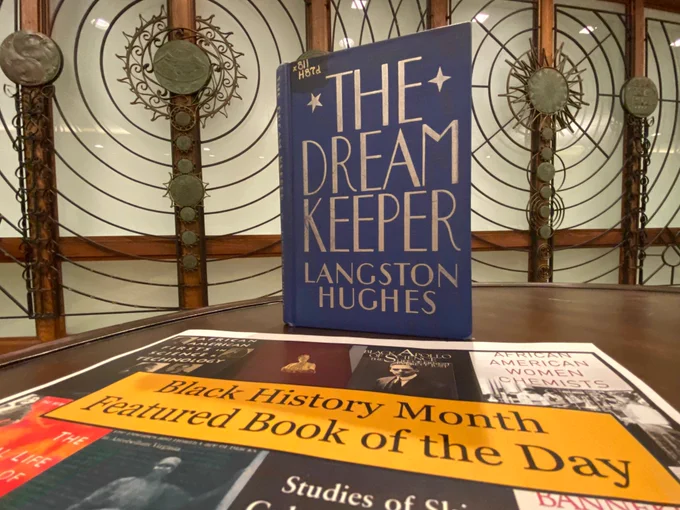 Photo of 1932 edition of The Dream Keeper by Langston Hughes: this book with blue cover and silver writing is visible on table near poster which reads “Black History Month Featured Book of the Day.”  The 5th Floor Special Research Collections screen is in the background.