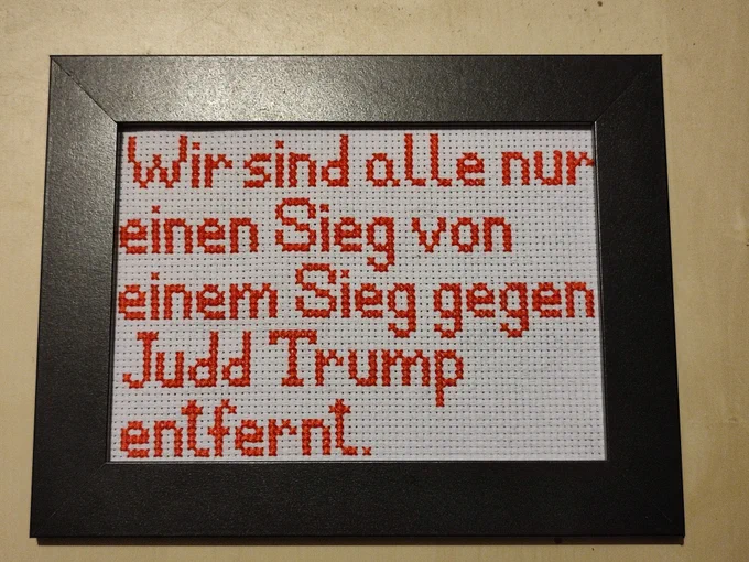 Fan-Art zu Ehren unserer 1.000 Folge. Ein gestrickter roter Schriftzug "Wir sind alle nur einen Sieg von einem Sieg gegen Judd Trump entfernt" auf weißem Hintergrund mit schwarzem Rahmen.