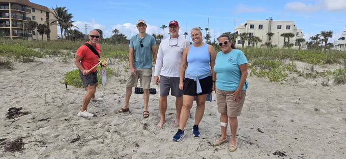 A group of individuals posing for a photo while planting sea oats on the beach. 