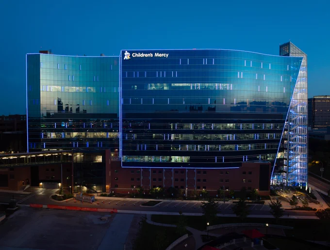 An outside photo of the Children's Mercy Research Institute at dusk. It's getting dark out. The building is lit up in blue.