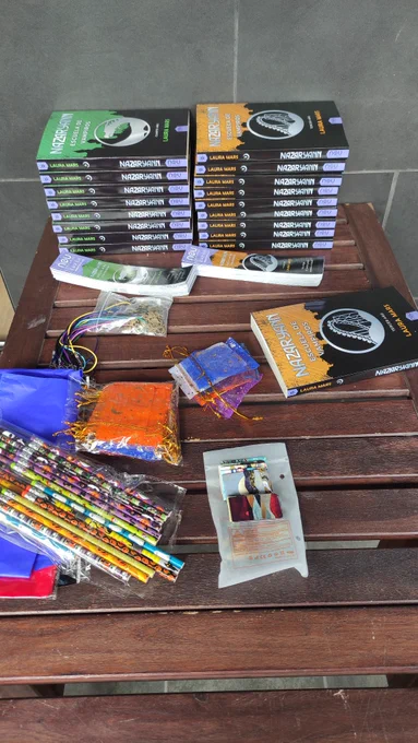 Foto a mi mesa, donde se ven los libros Nazaryann 3 y 4, mas los regalos distribuidos en montoncitos. Hay collares de dragón, lápices de Samhain, marcapaginas...