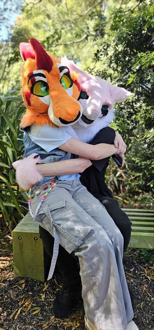 Two fursuits posing for a photo, one fursuiter sitting on the lap of the other