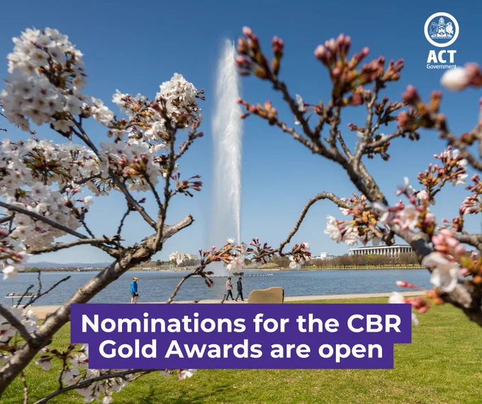Image featuring a vibrant scene with blooming cherry blossoms in the foreground and the Captain Cook Memorial Jet in Lake Burley Griffin, Canberra. A banner at the bottom announces 'Nominations for the CBR Gold Awards are open!'. Several individuals are visible enjoying the scenic view under a clear blue sky.