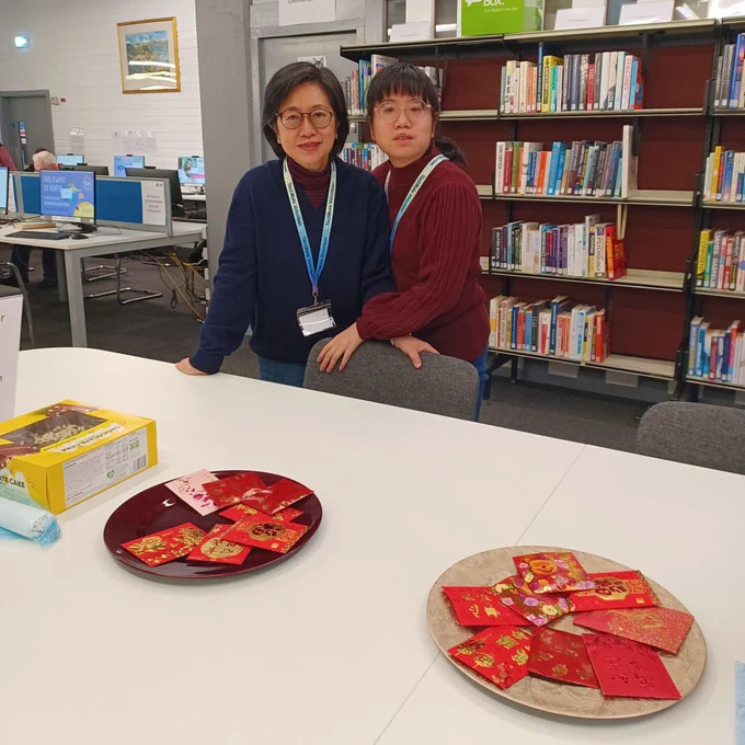 TechMates smiling with books behind them and a table with cake on in front of them.
