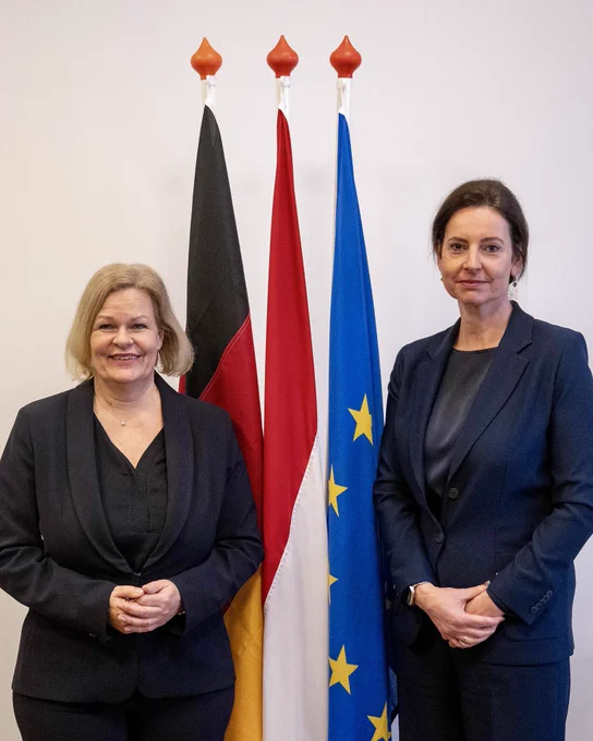Ministerinnen Faeser und Uitermark vor den Fahnen Deutschlands, der EU und der Niederlande.