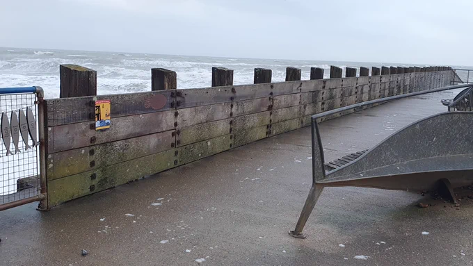 A stormy day at a seaside promenade, with strong waves hitting a long, weathered wooden sea wall called Splash Point groyne/