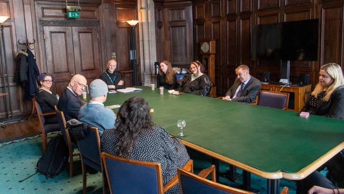 The group of UofG students and colleagues sitting round a table talking with John Swinney.