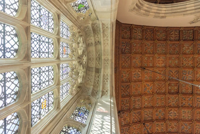 Interior view showing the intricate Gothic window designs and detailed patterned ceiling of the Yale university's Sterling Memorial Library.