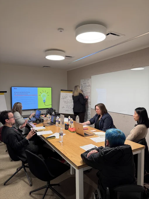 Image of individuals around table facing computer screen. 