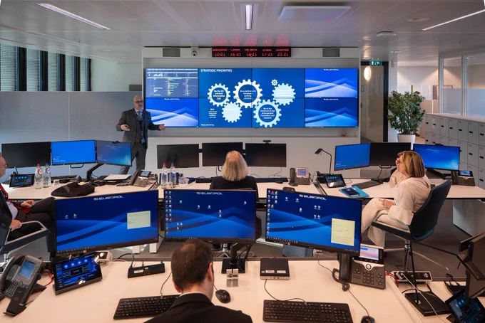 Blick ins Lagezentrum von Europol. Ein Mitarbeiter hält vor einem großen Monitor eine Präsentation.