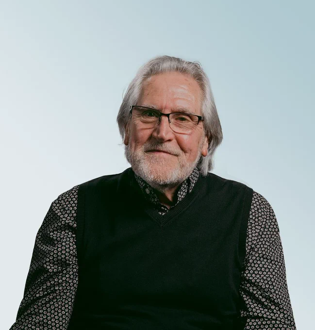 A photograph of Ted. He is wearing a black jumper and black and a grey shirt.

