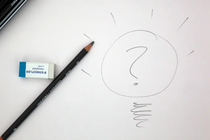 a photograph of a pencil and eraser sitting on a piece of paper, on the piece of paper there is a drawing of a lightbulb with a question mark in the centre