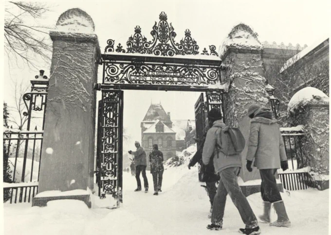 Individuals walking through a snow-covered ornate metal gate, with Brown University visible in the background during the Blizzard of 78.