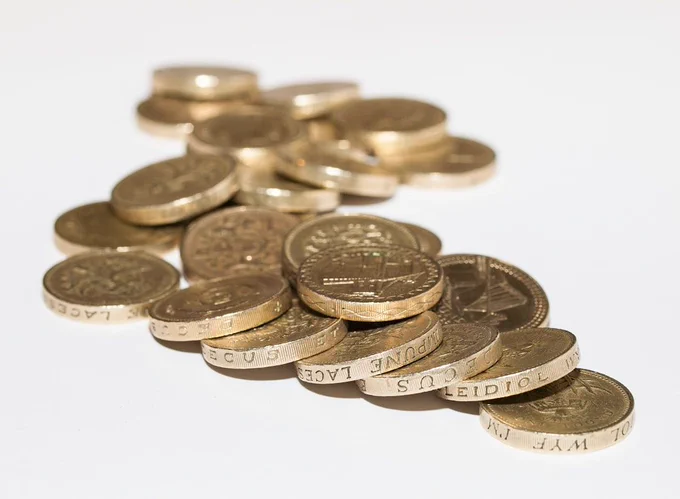 A photograph of a pile of one pound coins on a white table 