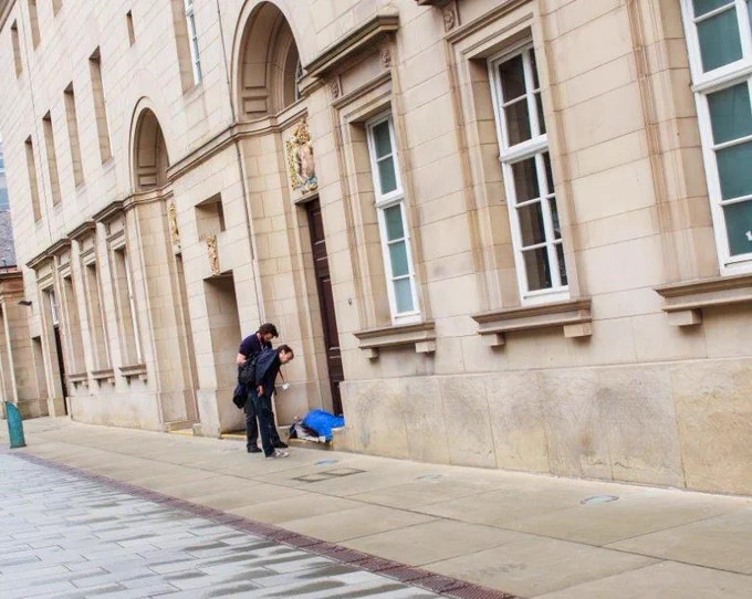 Outside Sheffield's City Hall two concerned people lean down to speak to a person sleeping rough.